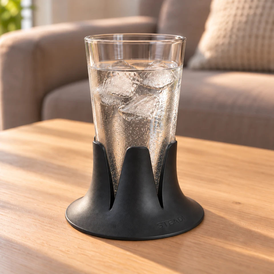 A clear tapered drinking glass filled with iced water, seated in a charcoal Steadi on a side table